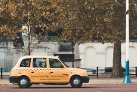 A yellow taxi drives through a tree-lined street in London, capturing the essence of urban autumn.